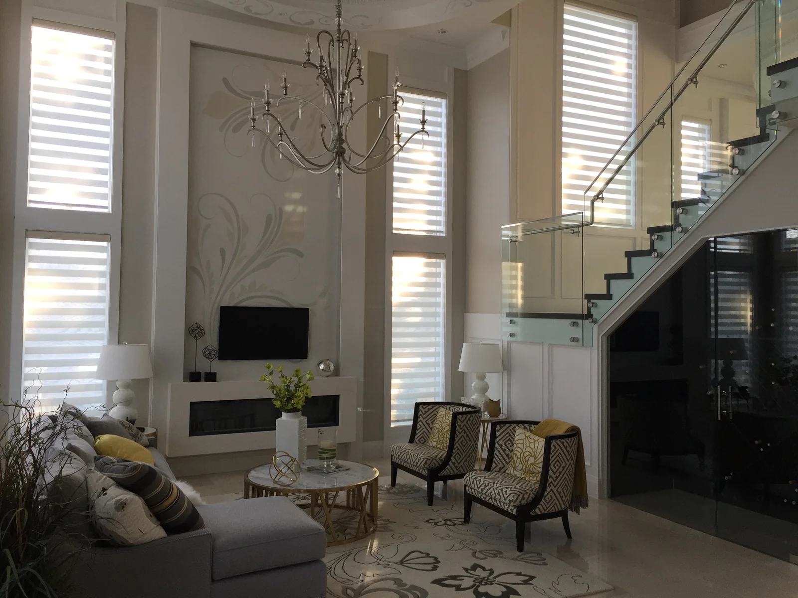Motorized zebra dual shades on two levels of tall windows beside a glass staircase